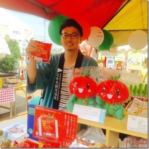 緑色のハッピを着た男性がトマトグッズを販売しているお店で商品を手に持っている様子の写真