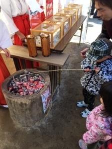 巫女さんの前の机の横に設置された木の入れ物で竿を持った男の子が釣りをしている写真