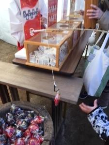 竿についた糸の針にかかった赤い魚のおみくじを手に取ろうとしている男の子の手の写真