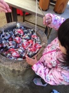 ピンクの上着を着ている女の子が鯛のおみくじを竿で釣っている写真