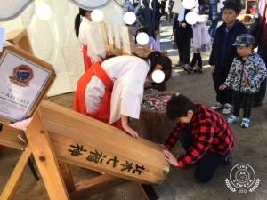 木製の大きなおみくじを手で押さえた巫女とくじを引いている男の子の写真