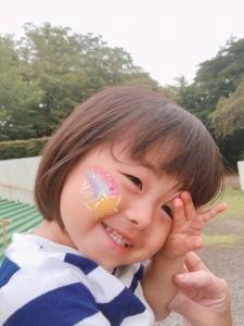 ほっぺに流れ星のペイントをつけて笑顔ではにかんでいる女の子の写真