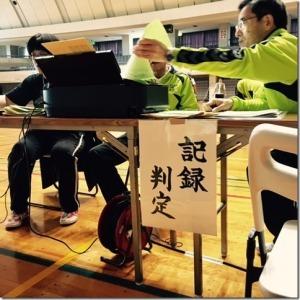 記録判定と書いた紙をつけてあるテーブルの上で作業する男性3名の写真
