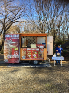 ケバブなどの商品の移動販売車と販売車の横で男性が料理をしている写真
