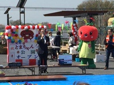 お手製のとまちゃん公園オープンと書かれた看板の前で挨拶をする北本市長ととまちゃんの写真
