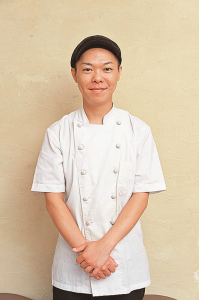 白いユニフォームを着て手を前に組んで写っている店長の佐藤さんの写真