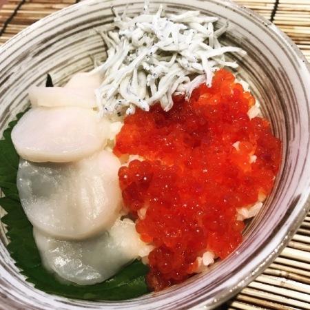 丸い丼の上に、ホタテの薄切り、真っ赤なイクラ、釜揚げしらすが敷き詰められた海鮮丼の写真