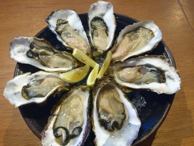 丸い皿に並べられた8個の新鮮な生牡蠣の写真