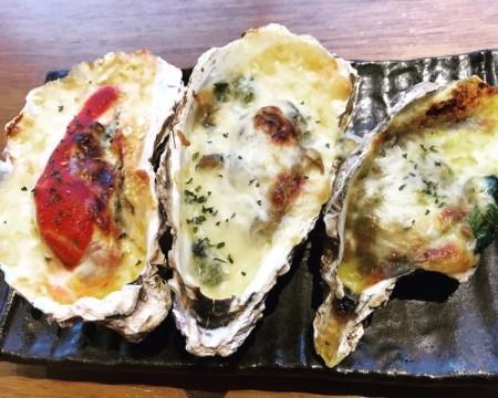 黒いお皿の上に、左からトマト、アンチョビ、カレー味の焼き牡蠣3個が盛り付けられた写真