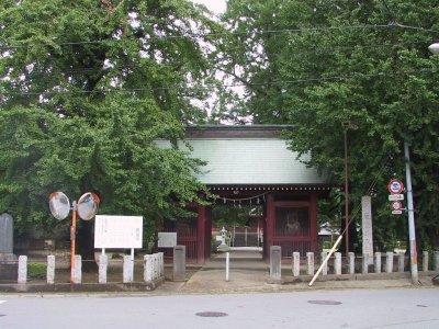 大きな緑の木に囲まれた屋根が緑で赤い門構えの真福寺門の写真