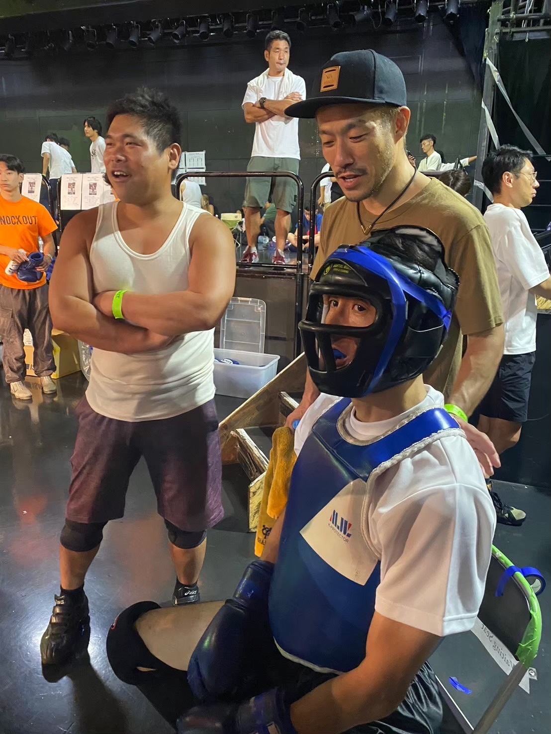 青い防具を身に着けてイスに座る男性選手と、その横に立つ2人の男性