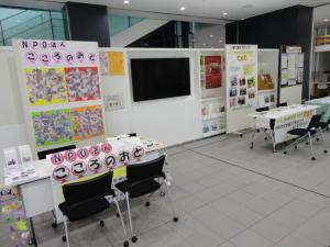 壁に資料が掲示されその前に対面で座る椅子とテーブルがある会場の写真