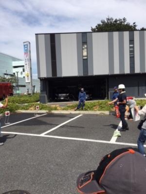 ヘルメットを着用した参加者が駐車場で的に向かって消化器で消火訓練をしている写真