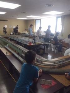鉄道模型を見つめる男の子の後ろ姿と数人の男性の写真