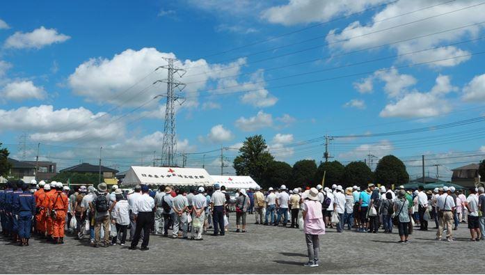 白い雲が広がる青空の下で防災訓練の会場に集まる大勢の参加者の写真
