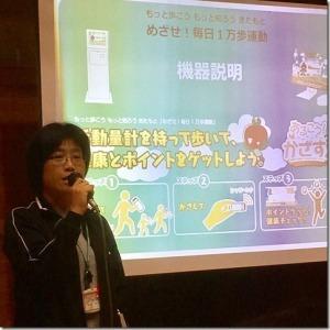モニターを使い、毎日1万歩運動の機器説明をしている女性担当職員の写真