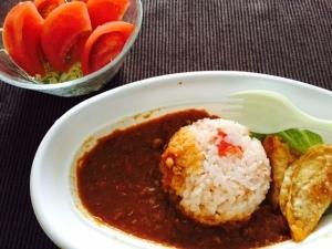 白いお皿にご飯と赤茶色のカレーが盛られている料理とトマトサラダの写真