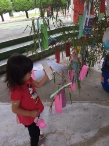 ミニーマウスの赤い洋服を着た女の子が願い事を書いた短冊を笹の葉につけている写真