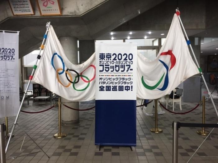 オリンピックの旗とフラッグツアーの看板とパラリンピックの旗が展示された写真