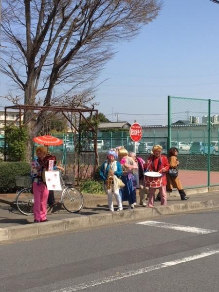 道を挟んだ道路沿いで演奏するちんどん屋さんたちの写真