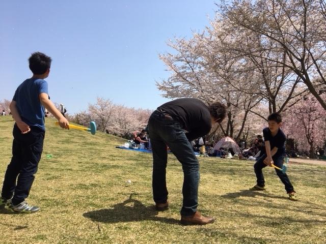 丘のふもとで2人の少年とお父さんが子供用ゴルフセットで遊んでいる様子の写真