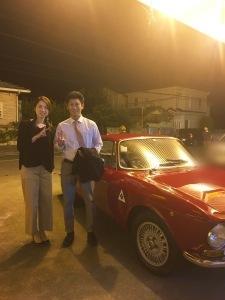 エキストラのご夫婦と赤い外車の写真