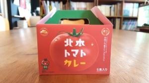 トマトの写真の上に北本トマトカレーと書かれたボックスが机に乗っている写真