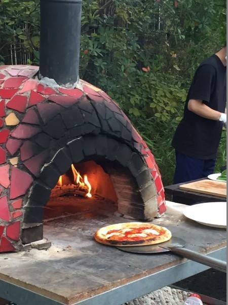野外でピザ窯にピザの生地を入れようとしている写真