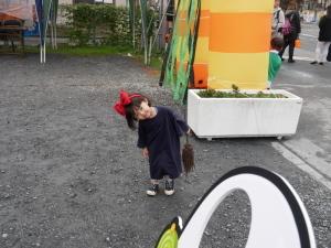 赤い大きなリボンを頭につけて黒のTシャツを着た女の子が小さなほうきを持って首をかしげている写真