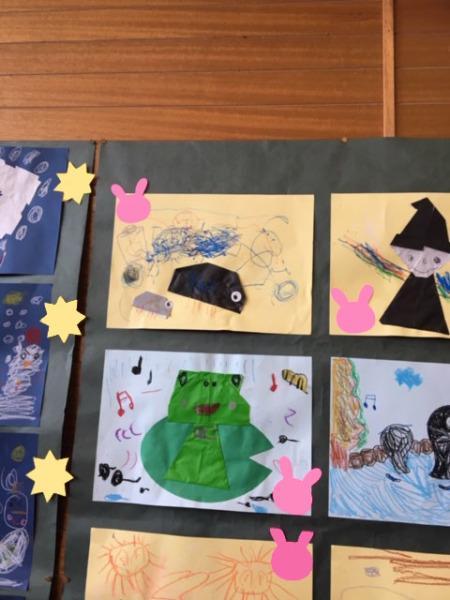お絵描きや折り紙で作った緑色のカエルや帽子をかぶった魔女等の作品が掲示されている写真