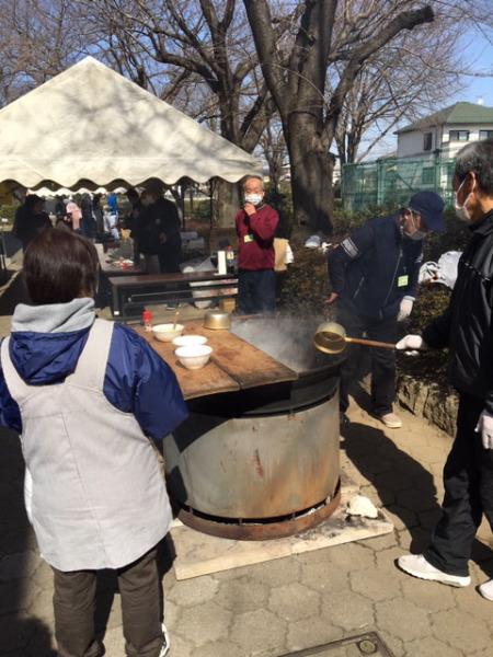 マスクをした大人たちが大きな鍋を使ってご飯を作っている様子の写真