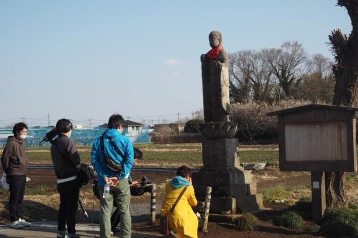 北地蔵の前で手を合わせている金子さんのロケ風景の写真