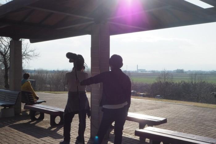 高尾さくら公園から目の前に広がる広大な畑の風景を眺めている金子さんとその様子をカメラに収めているカメラマンと音声さんの写真
