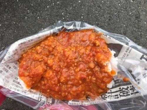 アルファ米とトマトカレーが、ビニール袋をかぶせた新聞紙の皿の上に盛られている写真