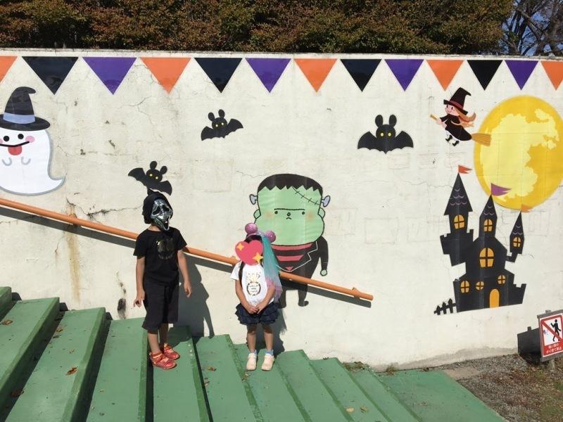 壁にオバケとこうもりとお城のイラストがある壁の前に仮装した2人の子供が立っている写真