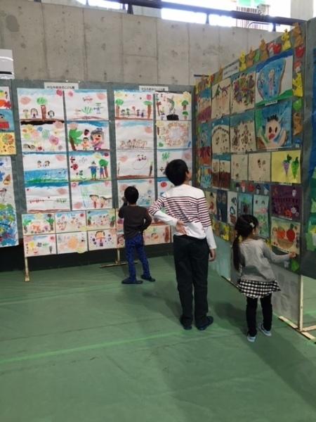 小学生の絵画作品が展示され小さな子供たちが見ている写真