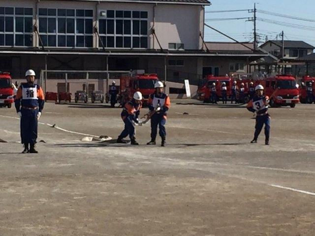 直立する指導者1名とホースを持つ3名の消防団員の写真