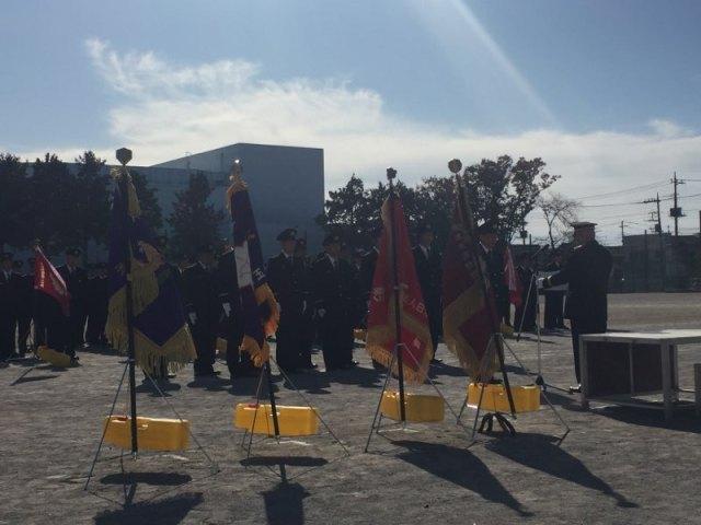 朝礼台の横に並べられた4本の優勝旗と表彰される消防団員の写真
