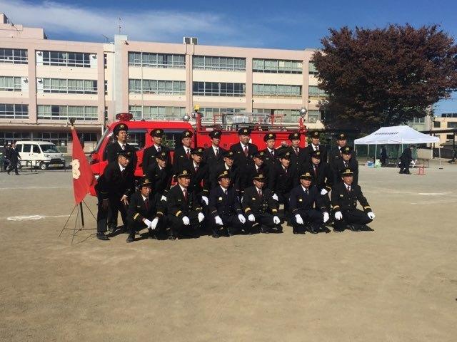 消防車の前で記念写真を撮る大勢の消防団員の写真