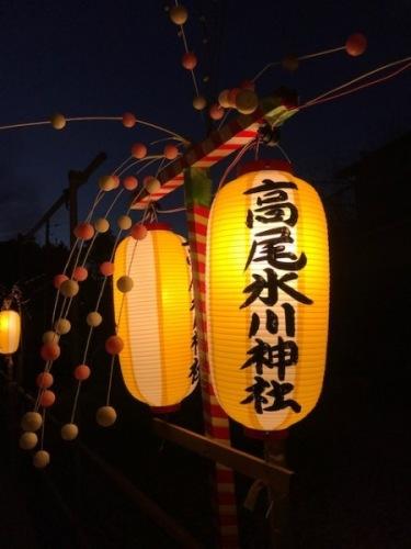 高尾氷川神社と書かれ黄色と白の提灯と白とピンクの餅花の写真
