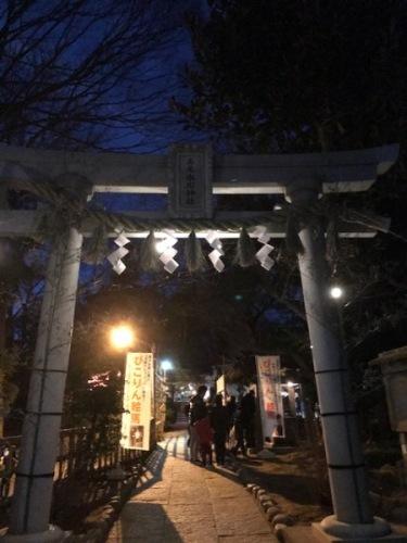 夕暮れの中、明るくライトアップされた参道と高尾氷川神社鳥居の写真