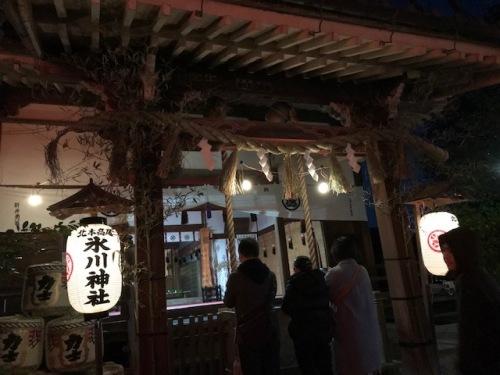 両側に高尾氷川神社の提灯が灯る拝殿の前で参拝をする3人の写真