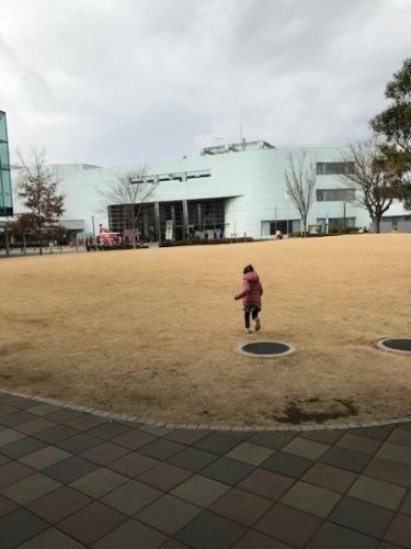文化センター前の芝生の上を、センター出入口前に止められた赤い車に向かって駆け出す女の子の写真