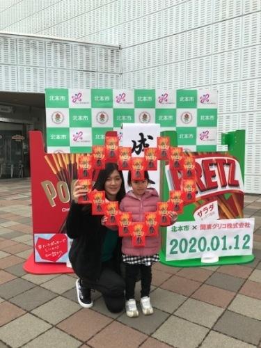 2020年01月12日の日付が入ったポッキーとプリッツのフォトブース前で、ハートのポッキーを持ったリポーターと娘さんの写真