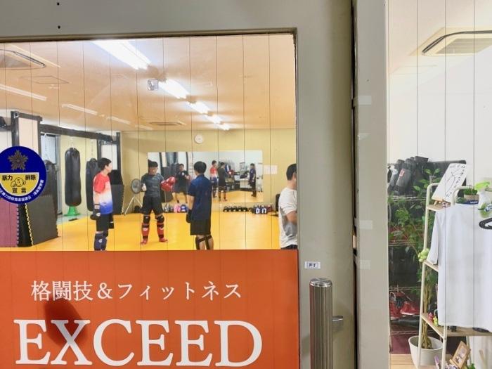 ジム出入口のガラス越しに4名の男性がグローブをつけトレーニングしている様子の写真