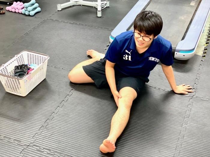 メガネをかけた男性スタッフが、床の上で左足を伸ばしストレッチをしている様子の写真
