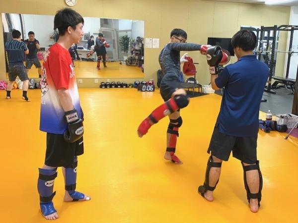 ローキックの練習をしている1組のペアと、それを見学している1人の男性会員の写真
