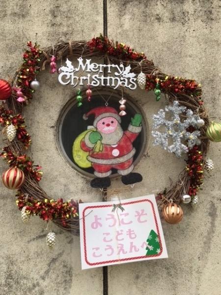 サンタクロースの絵と「ようこそ こどもこうえんへ」の文字がクリスマスリースに飾られている写真