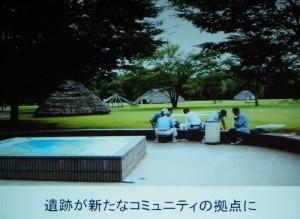 水子貝塚公園内にて遺跡を背に5名の男性が座りながら語り合っている写真