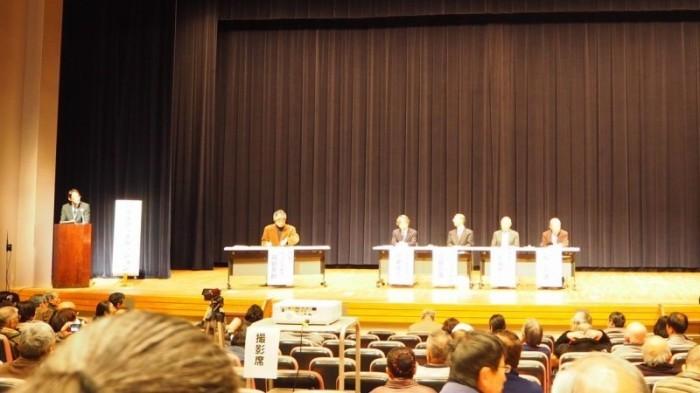 司会者と5人の専門家が壇上にて講演を催している様子の写真